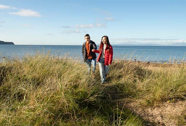 A couple walking along a Scottish beach in Autumn
