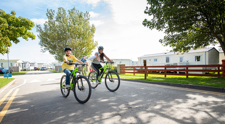 A family riding bikes on a sunny day through Ty Mawr Holiday Park