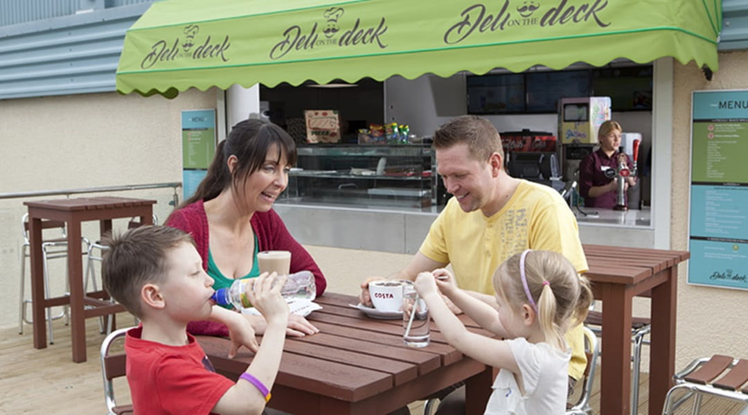A family enjoying drinks on the terrace at Deli on the Deck at Trecco Bay Holiday Park in Wales