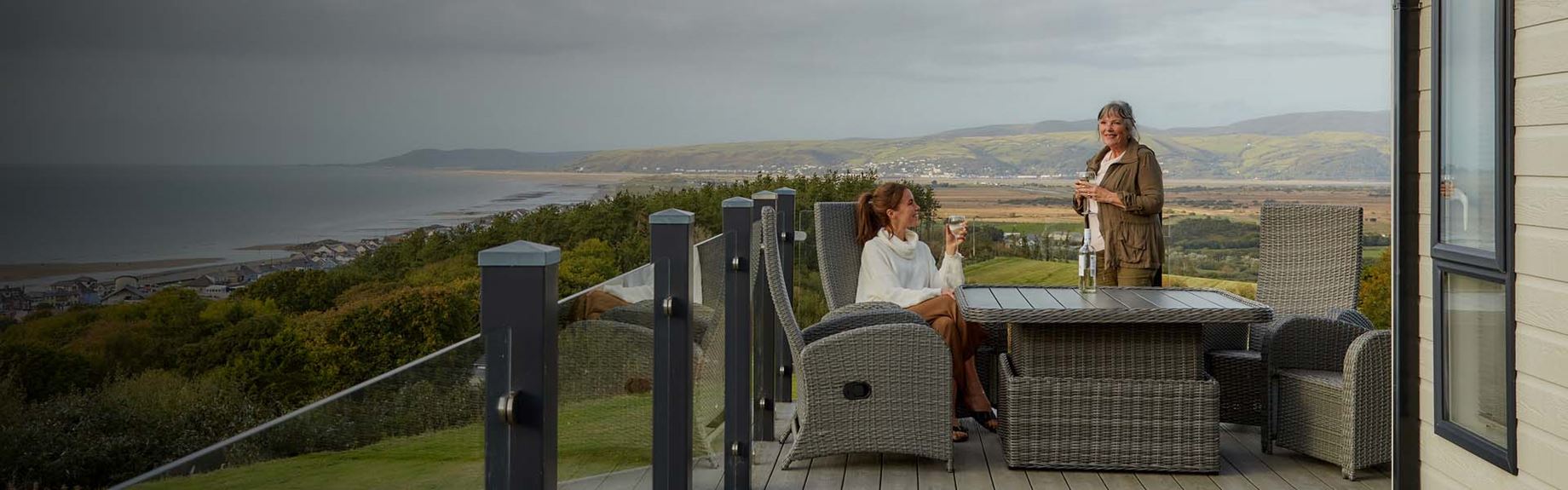 A mother and daughter taking in the views from their holiday lodge veranda overlooking the Welsh coast