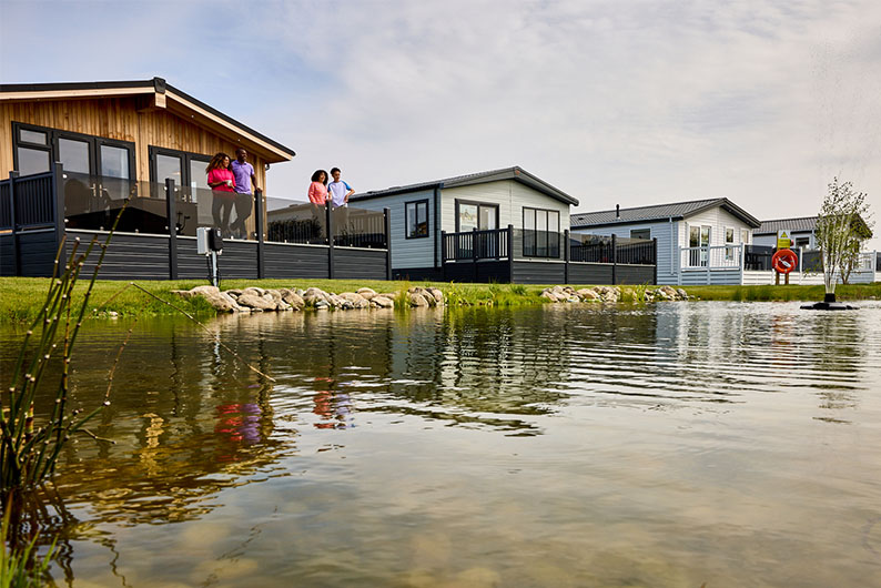 A row of luxury lodge holiday homes for sale overlooking a pond at Ty Mawr Holiday Park in North Wales