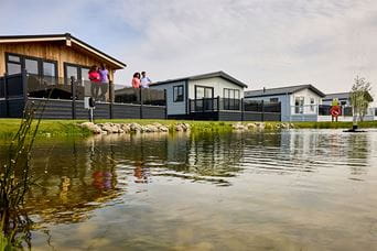 A row of luxury lodge holiday homes for sale overlooking a pond at Ty Mawr Holiday Park in North Wales
