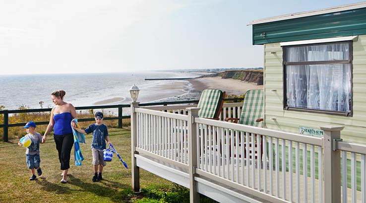 A family walking across the grass by a caravan with a veranda on the sea front at Barmston Beach