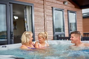 Parents and a girl sitting in a hot tub outside their holiday lodge