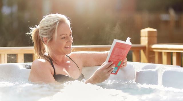 A woman relaxing in a hot tub reading a book