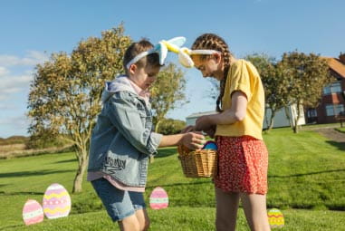 Girls wearing bunny ears sharing Easter eggs from a wicker basket