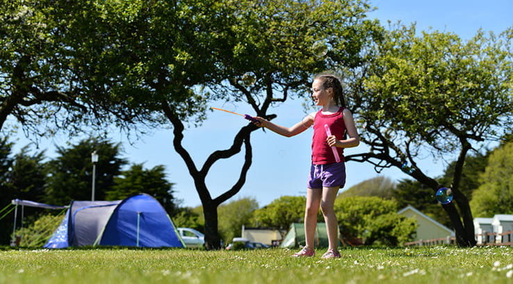 girl playing with bubbles outside a tent on a sunny day