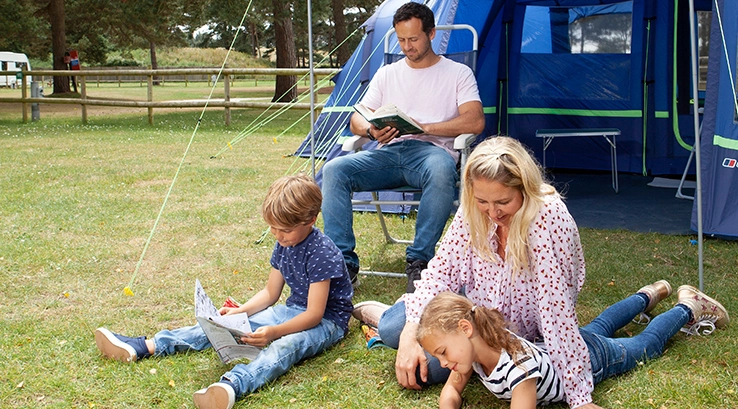 family reading books and magazines sat outside tent in sunshine
