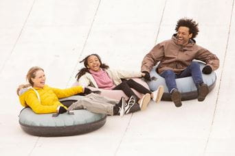 two young kids and an adult in ring tubes on the ski slope