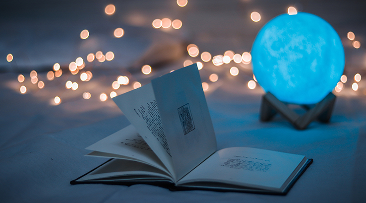 A book lying open by a crystal ball and fairy lights