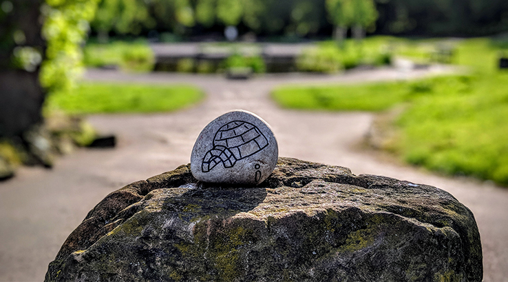 A pebble with pebble art drawn on it balanced on a rock