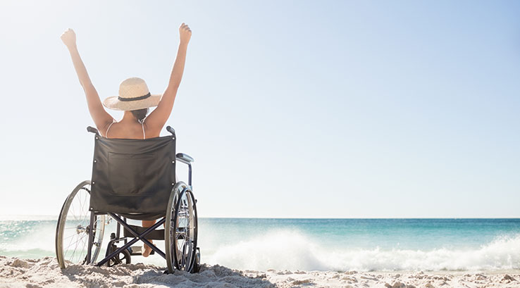 A woman sitting in a wheelchair looking out to sea on a sandy beach