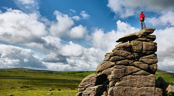 A man standing on top of a rock formation at Hound Tor, Devon