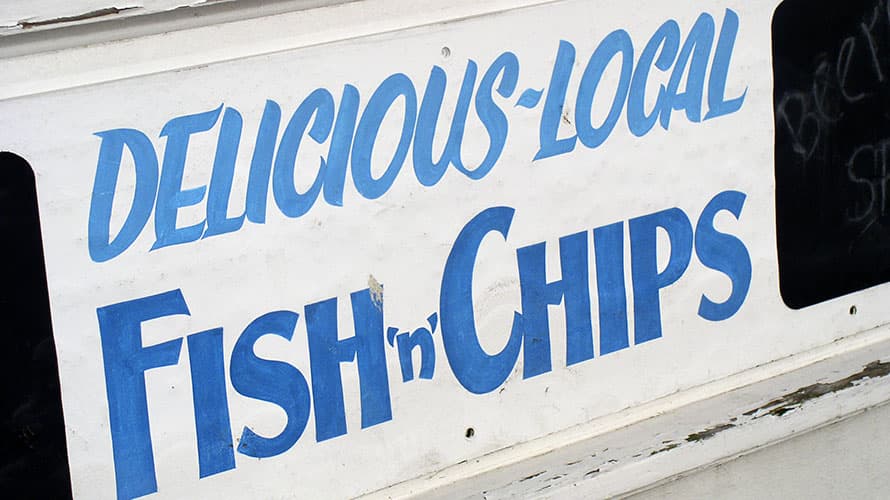 A traditional painted wooden sign advertising delicious and local fish and chips