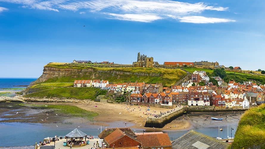 A vibrant photo of Whitby Harbour, with the ruins of the cathedral visible on the hilltop behind