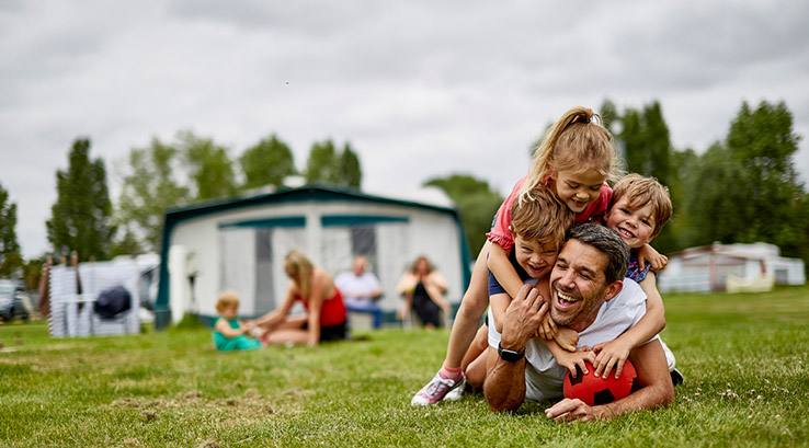 A father playing with his kids on the grass outside a pitched up awning