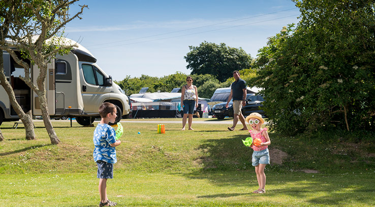 Kids playing on the grass whilst parents watch by the touring pitches at Holywell Bay