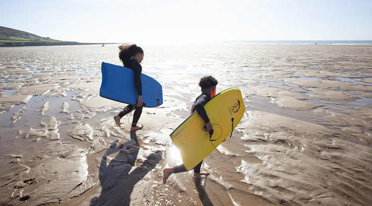 Two children running across Croyde Bay Beach with surfboards