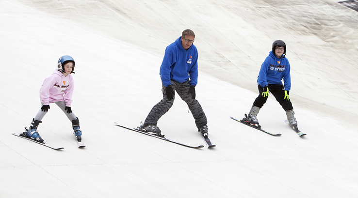 A ski instructor teaching two children how to ski down a dry ski slope at Warmwell Holiday Park