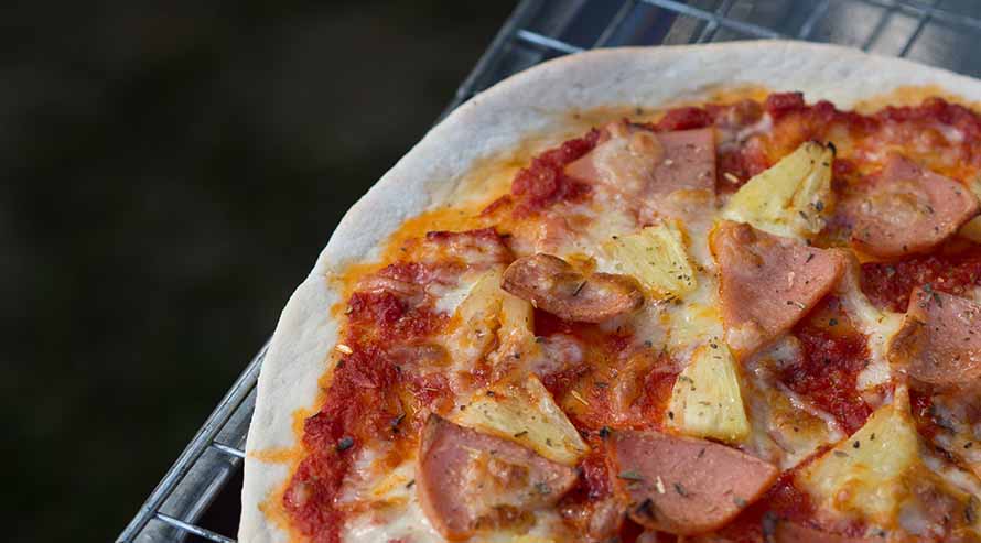 A ham and pineapple pizza cooling on a grill
