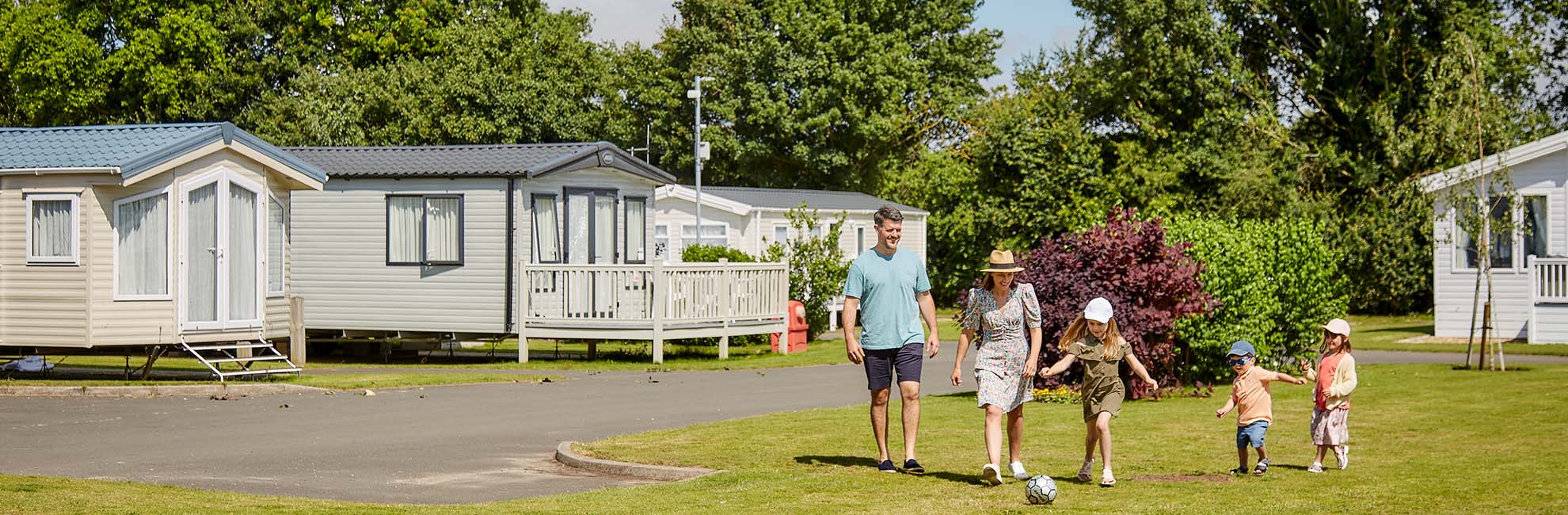 A family running across the grass with a football at Breydon Water Holiday Park