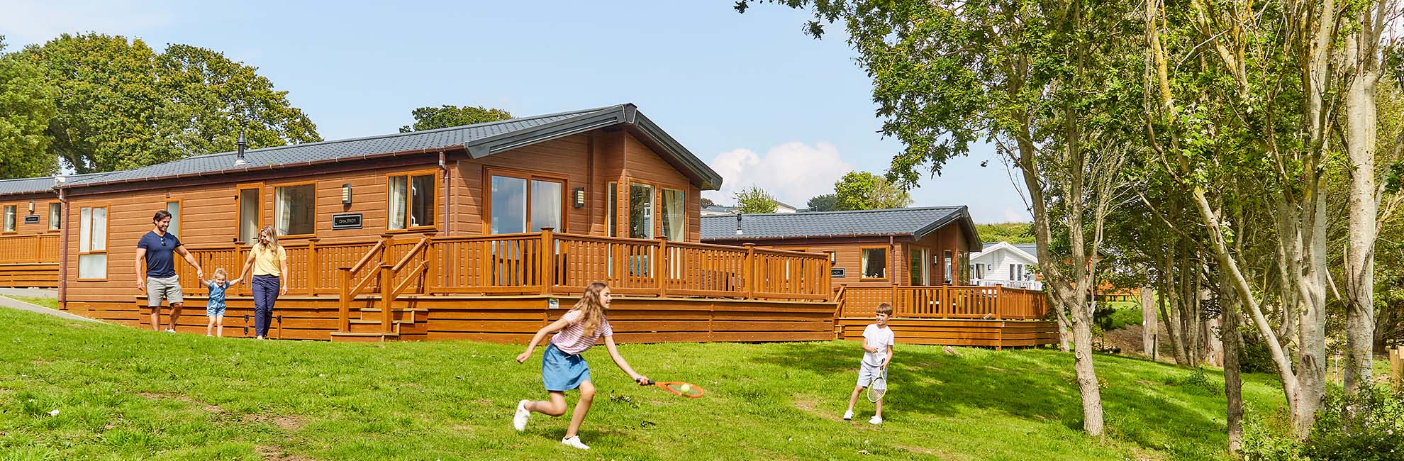 A family playing on the grass outside their lodge at Nodes Point Holiday Park