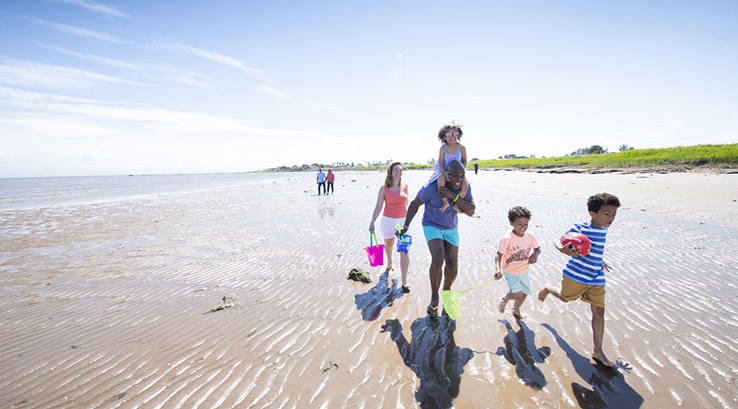 A family running across a sandy beach on a summer's day