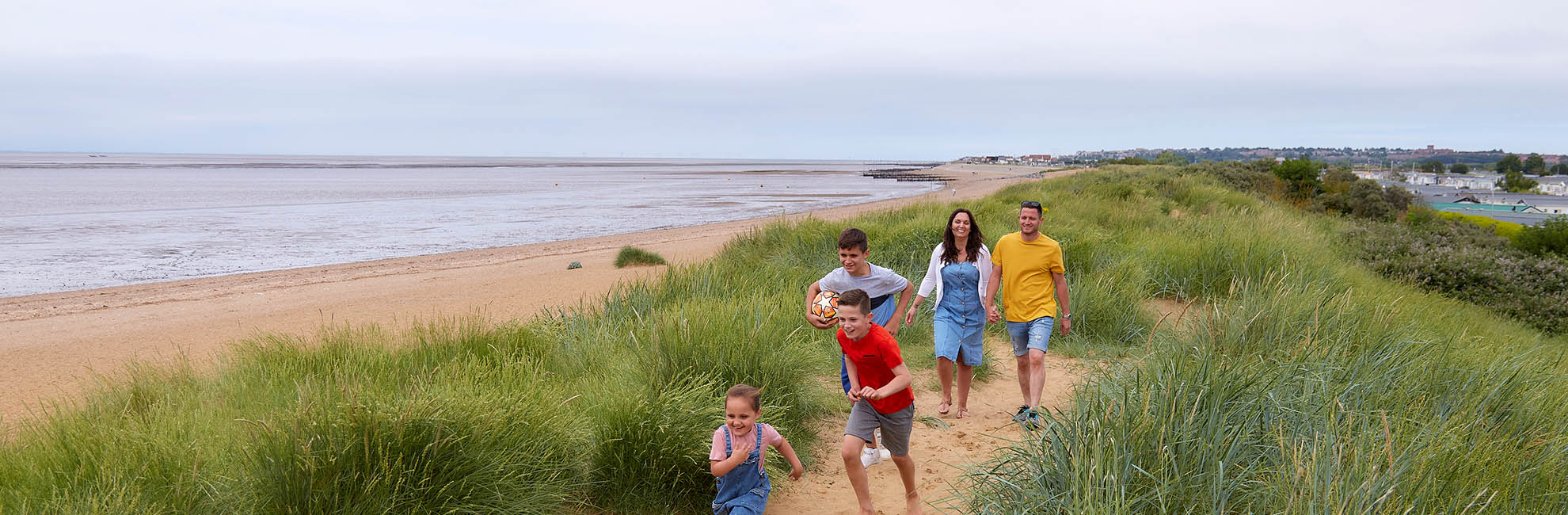 A family running through the sand dunes at Heacham Beach