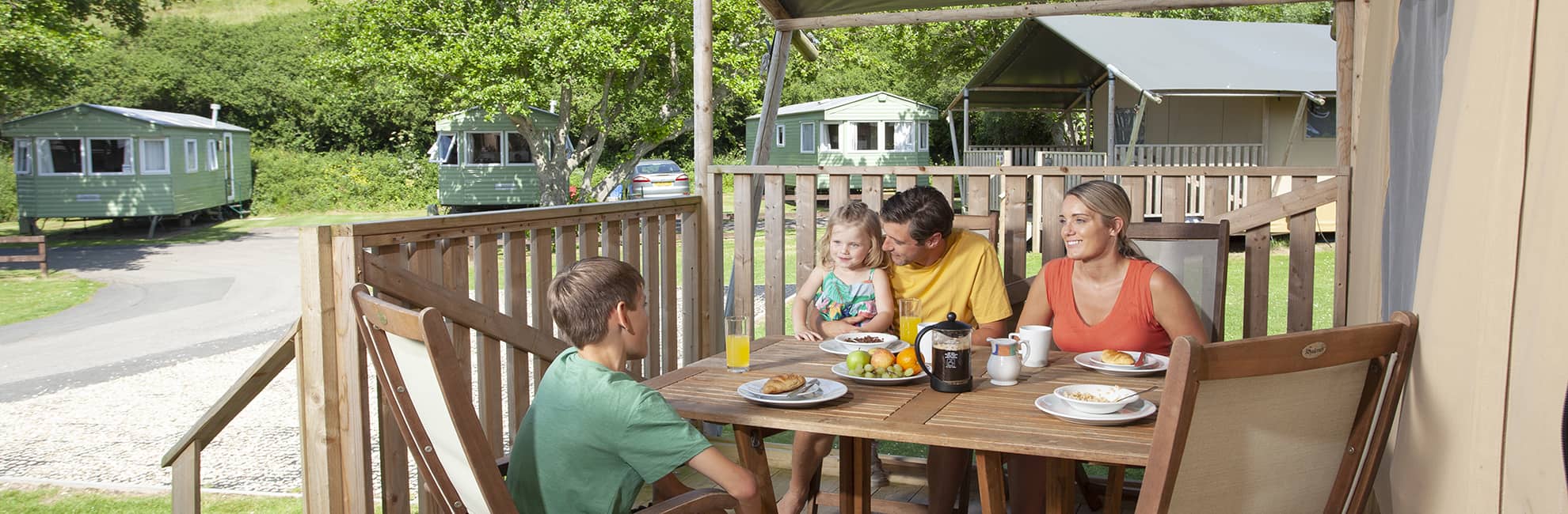 A family relaxing with food and drinks on the veranda of their glamping Safari Tent