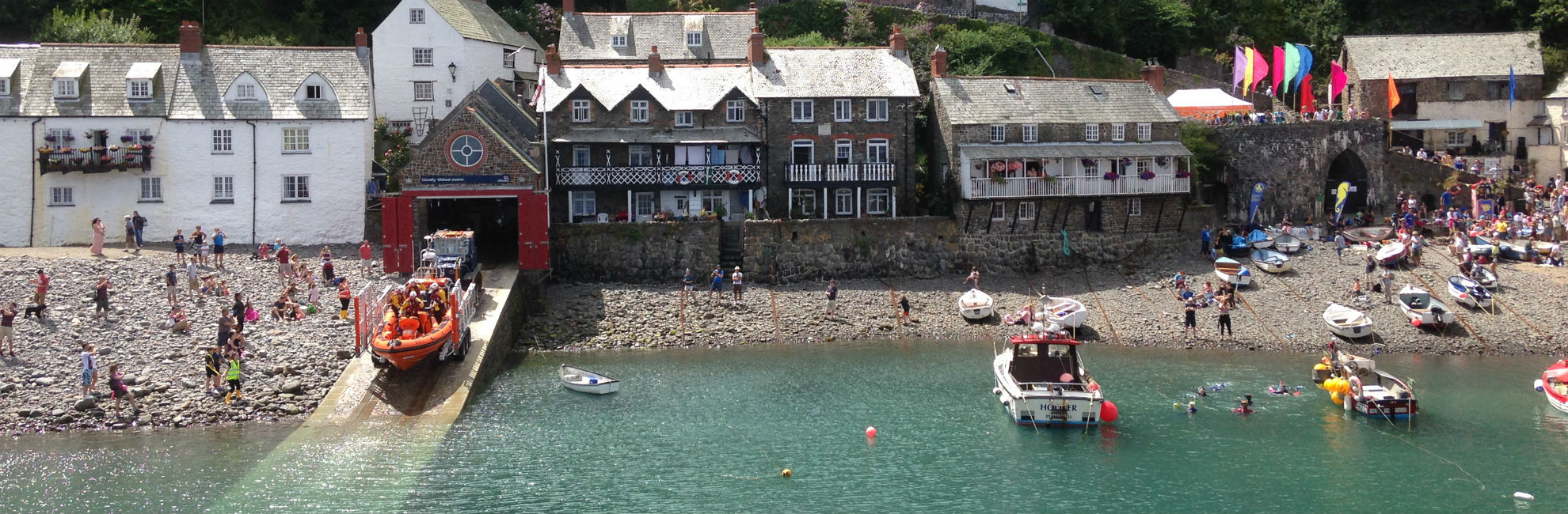 A busy summer day at Clovelly Harbour with tourists on the beach and boats launching from the slipway