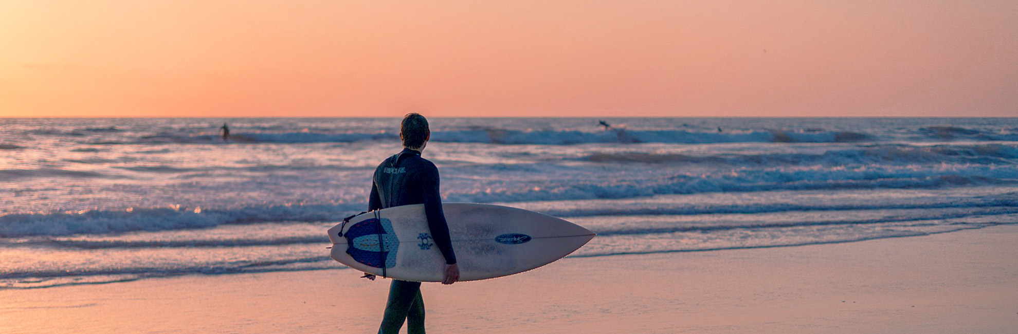 A surfer walking along a beach in Devon at Sunset