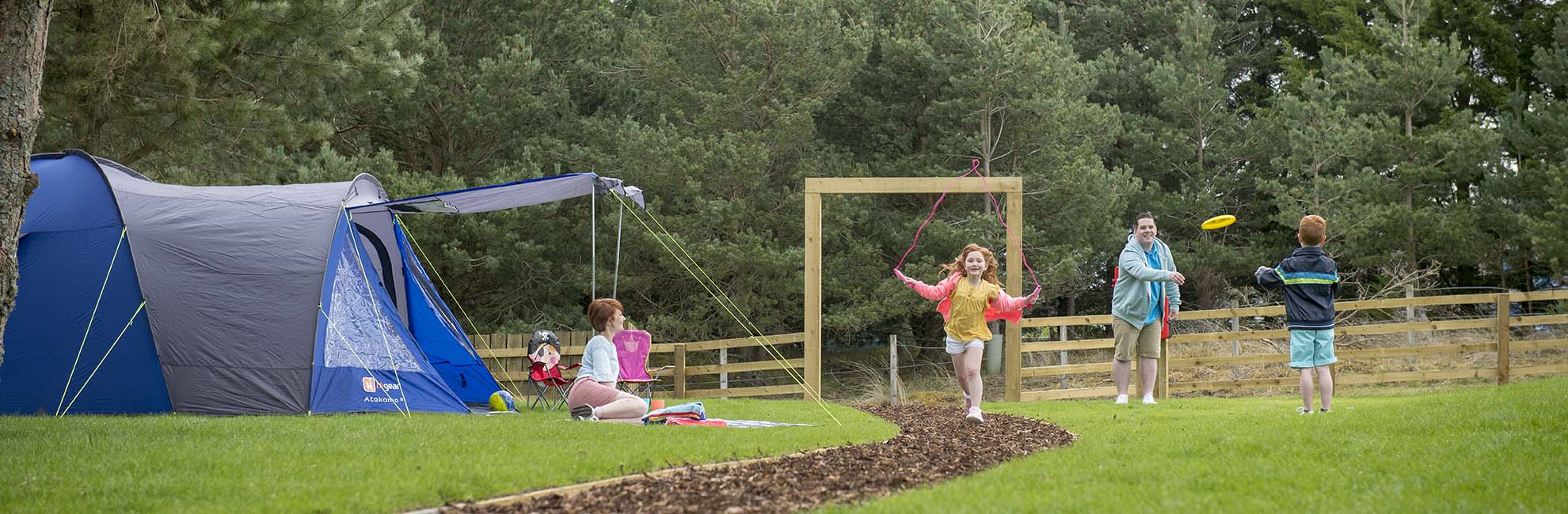 A family playing frisbee on the grass outside their tent at a Parkdean Resorts campsite in  Scotland
