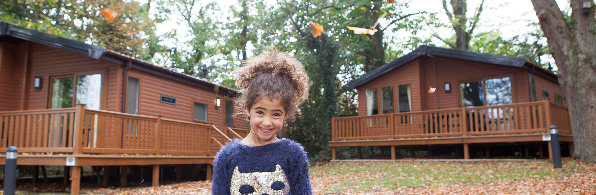 A girl smiling outside wooden lodges in the autumn