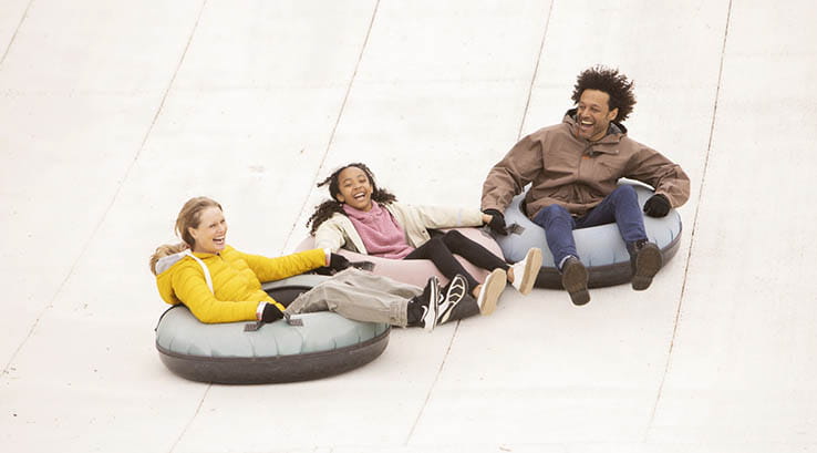 A family riding down a dry ski slope in inflatable rings
