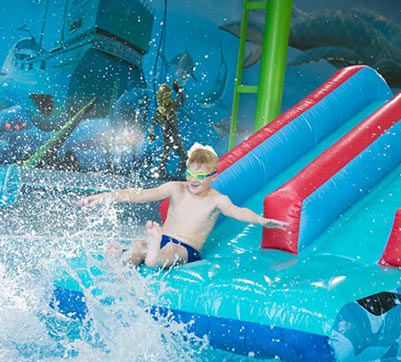 A boy sliding down an inflatable slide into an indoor swimming pool making a big splash
