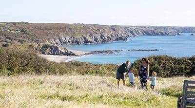 A family walking across a grassy area of Sea Acres Holiday Park with the sea in the background