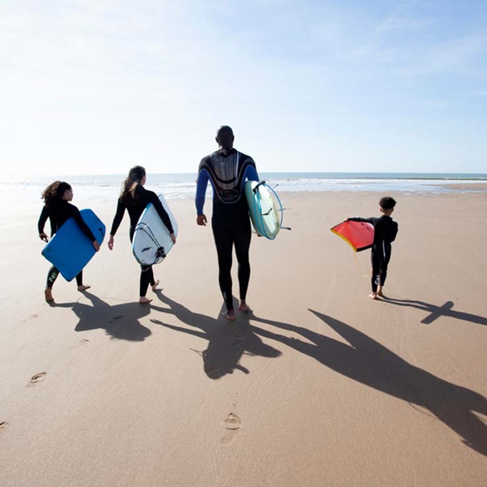 A family walking along the beach with surfboards