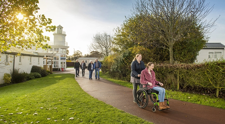a woman being pushed in a wheelchair through a holiday park