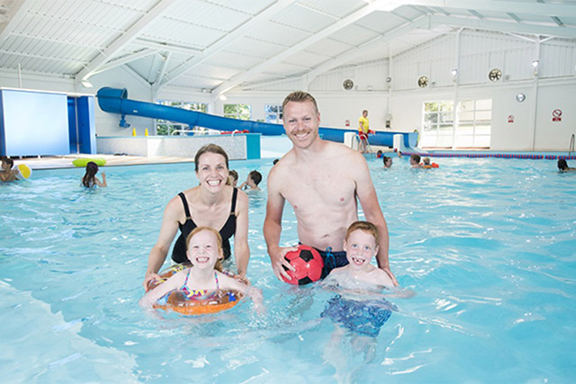 A family smiling into the camera in the indoor swimming pool