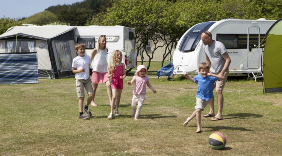family playing ball games outside a tent and touring caravan