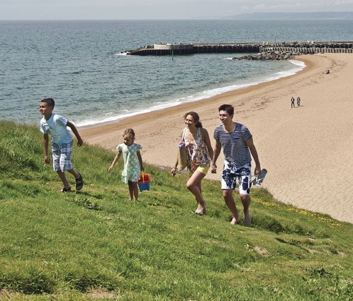 A family walking up a grassy field next to West Bay beach