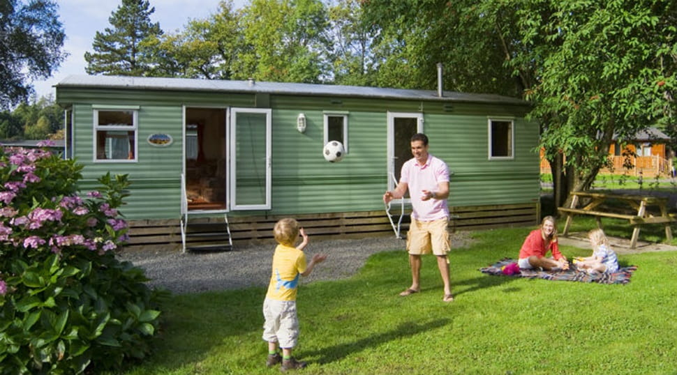 A family playing with a football and relaxing on the grass outside their caravan