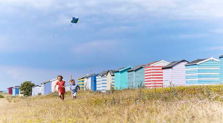Children flying a kite over the beach huts at Greatstone Beach